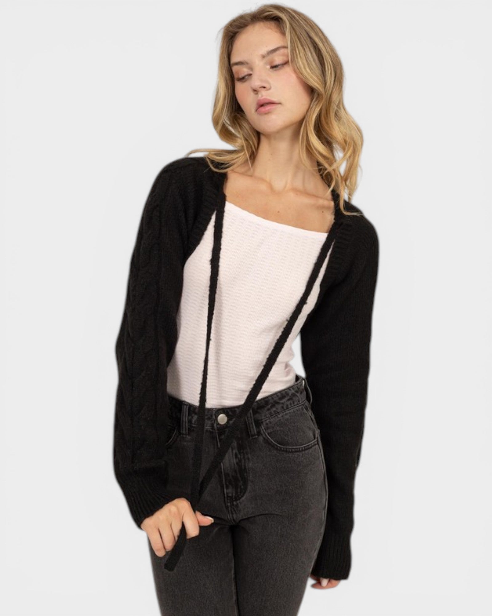Woman wearing a black cardigan over a white top and black jeans on a white background