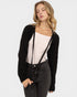 Woman wearing a black cardigan over a white top and black jeans on a white background