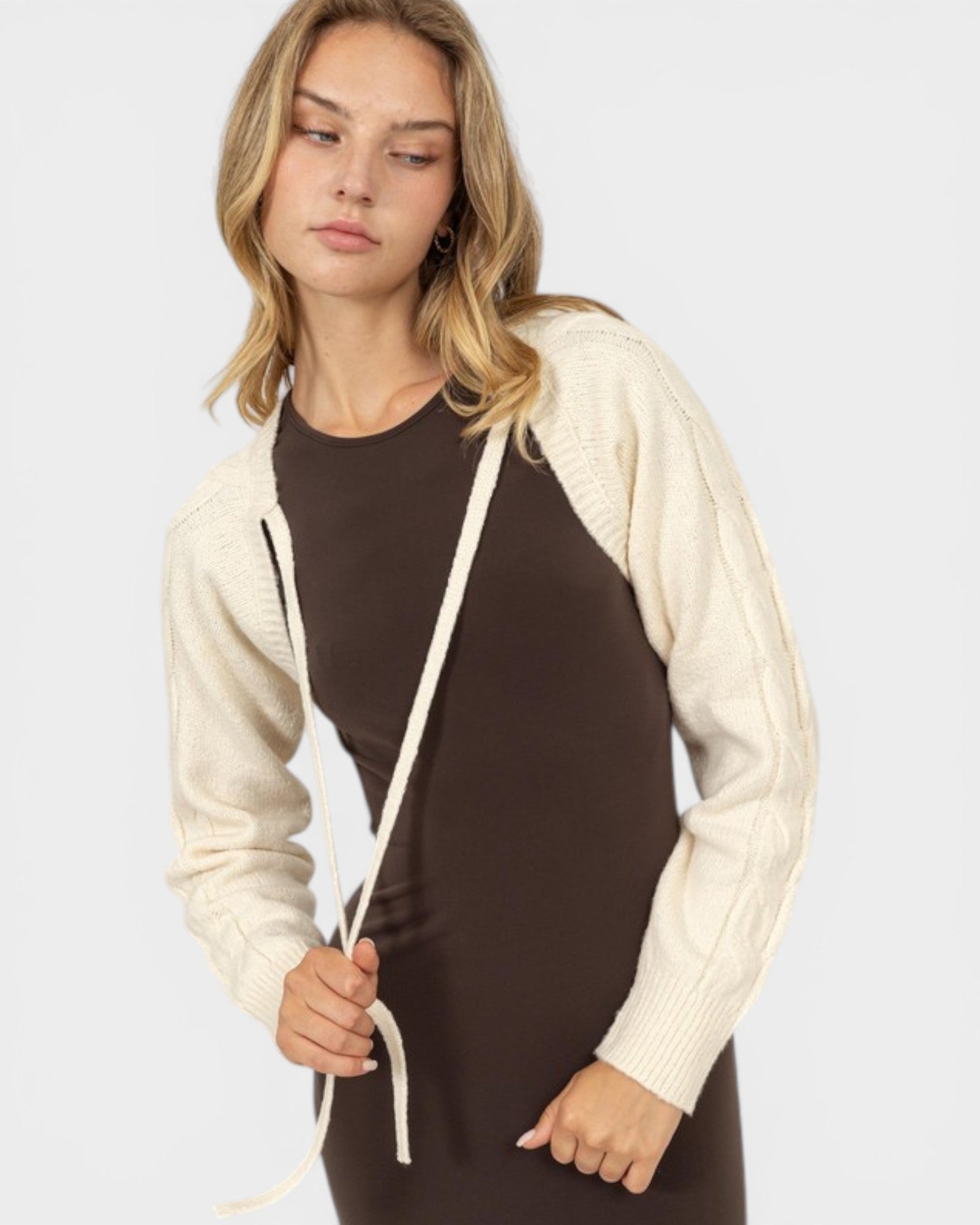 Woman wearing a cream cardigan over a brown dress on a white background