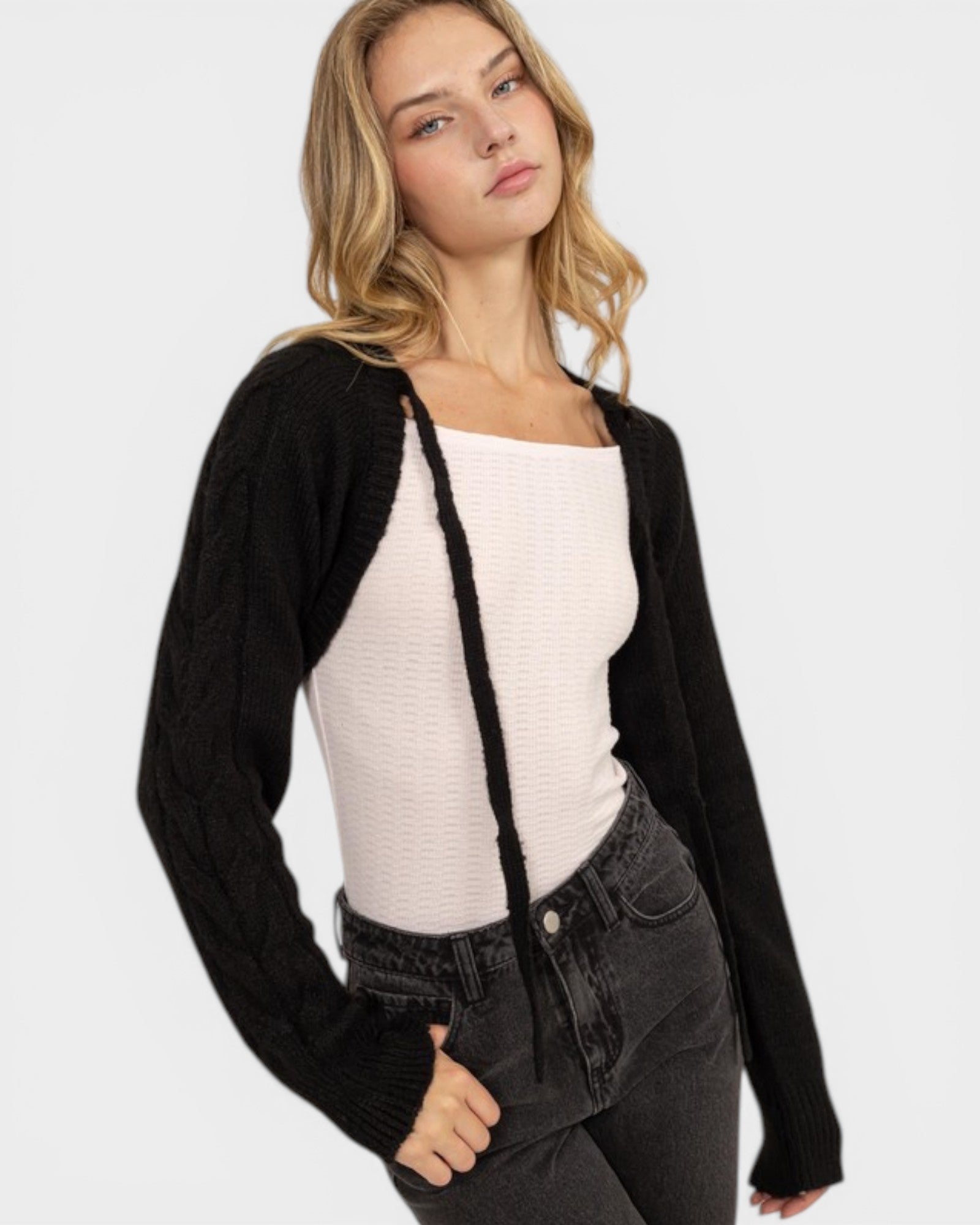 Woman wearing a black cardigan over a white top and dark jeans on a light gray background