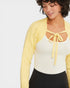 Woman wearing a yellow cardigan over a white top with a bow, on a light gray background