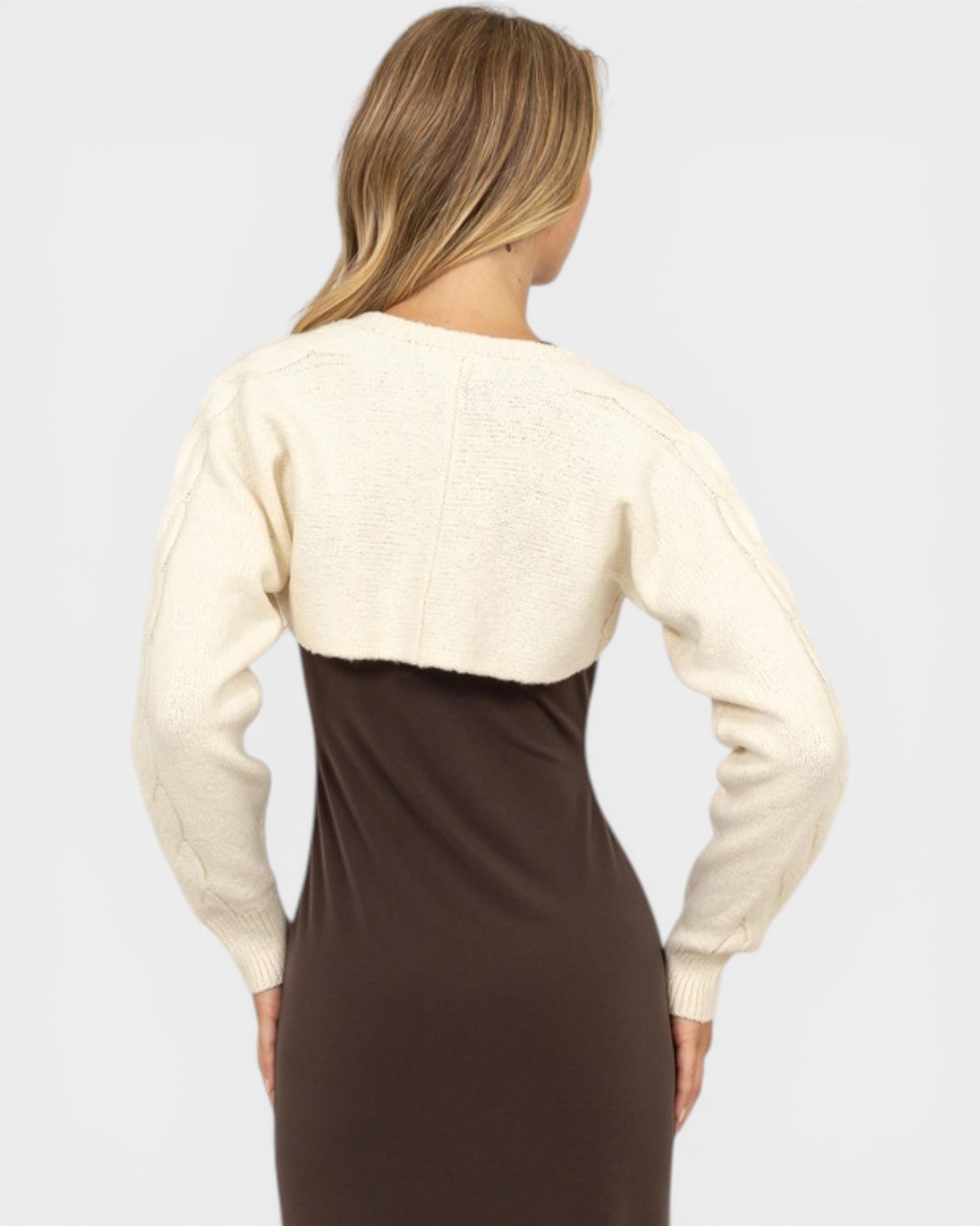 Woman wearing a cream cardigan over a brown dress on a plain background