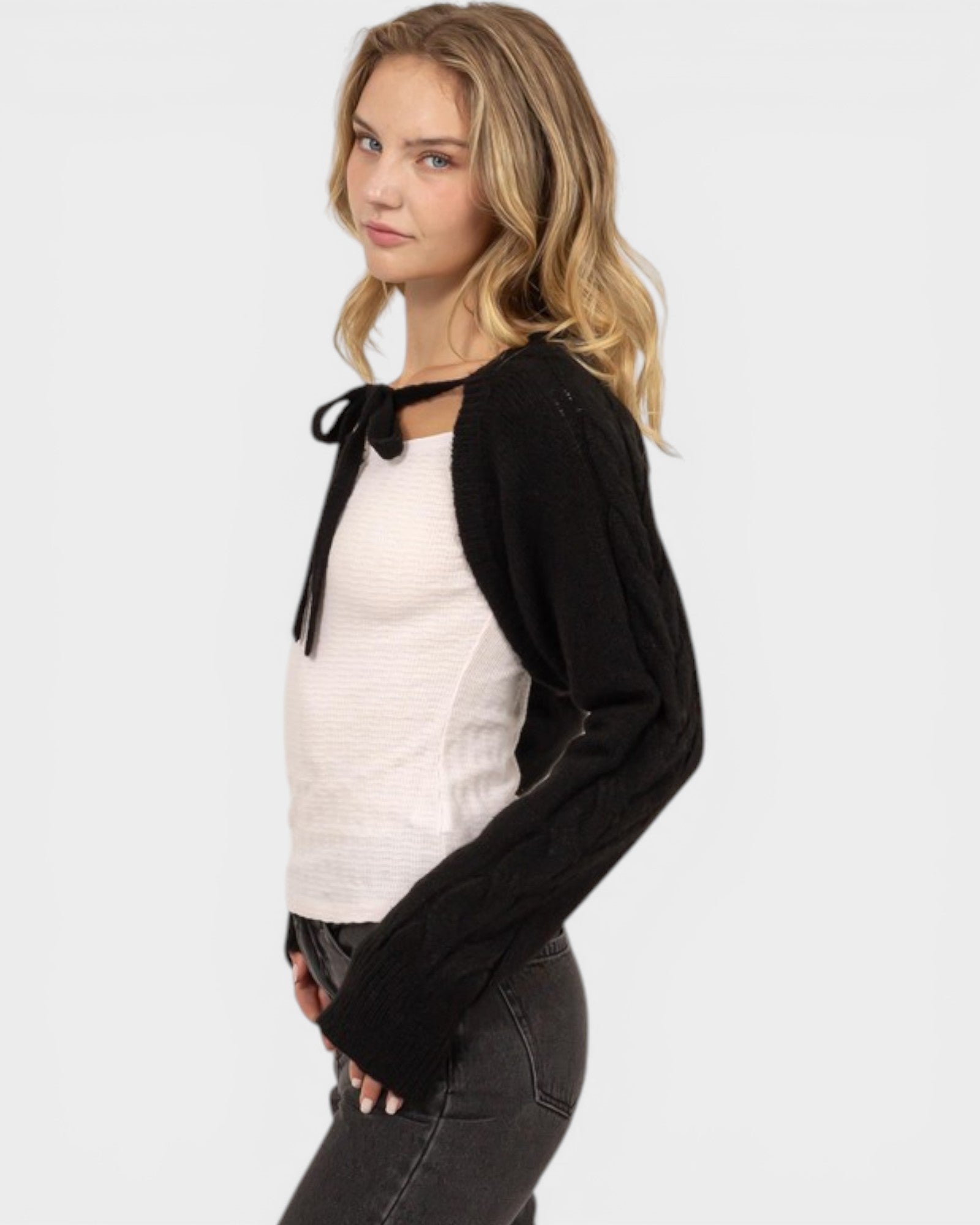 Woman wearing a black cardigan over a white top with a bow tie, on a plain background