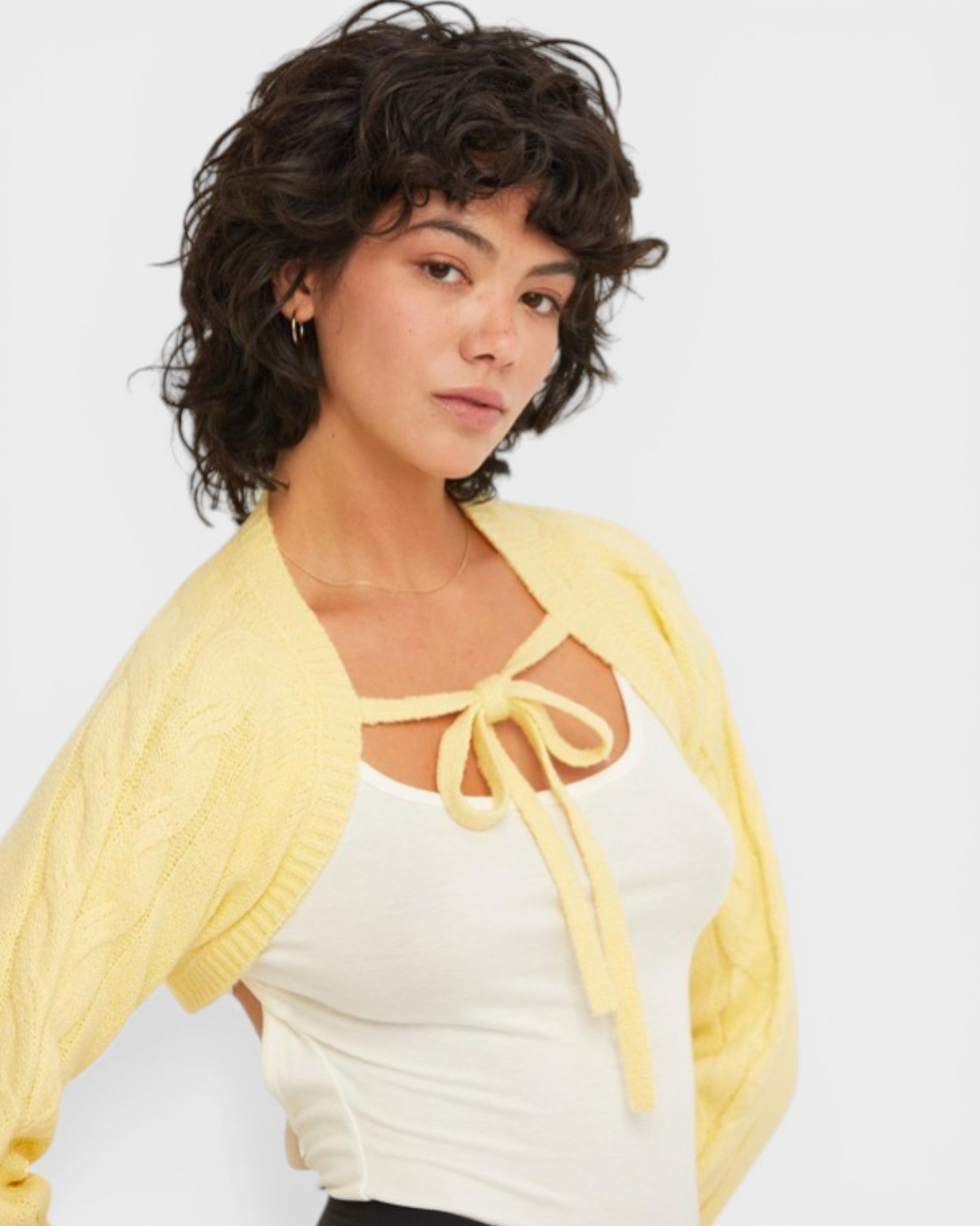 Woman wearing a yellow cardigan over a white top on a plain background