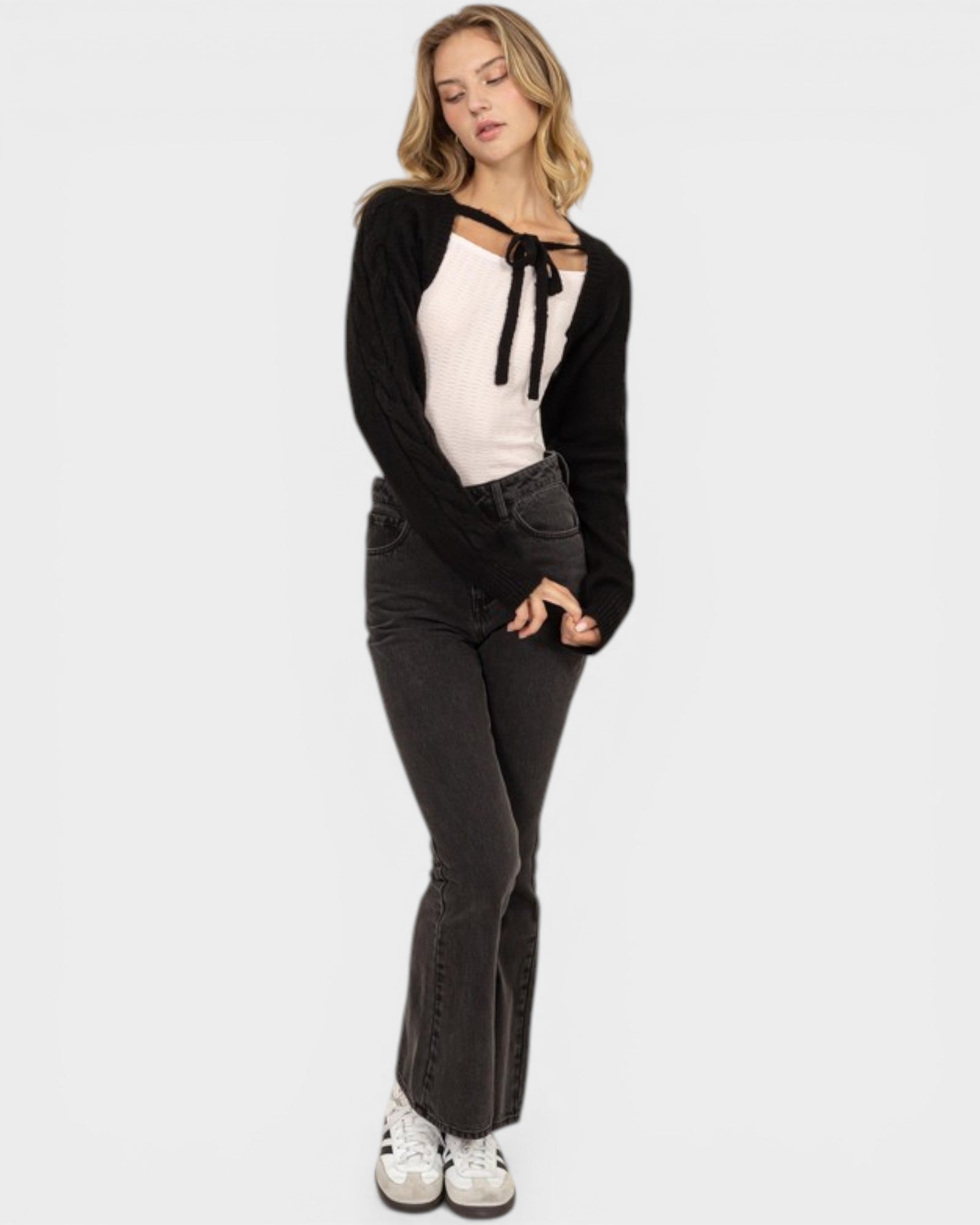 Woman wearing a black cardigan, white top, and dark jeans on a white background