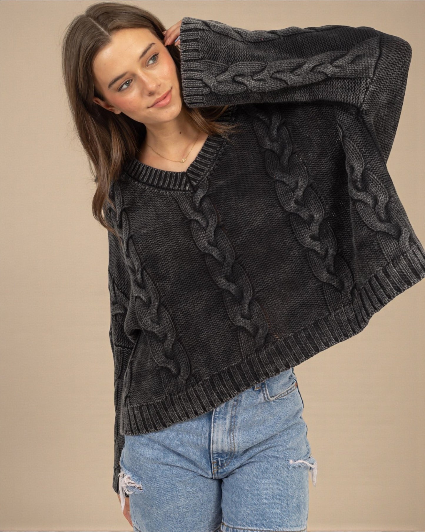 Woman wearing a dark gray cable knit sweater with ruffled details on a beige background