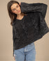 Woman wearing a dark gray cable knit sweater with ruffled details on a beige background