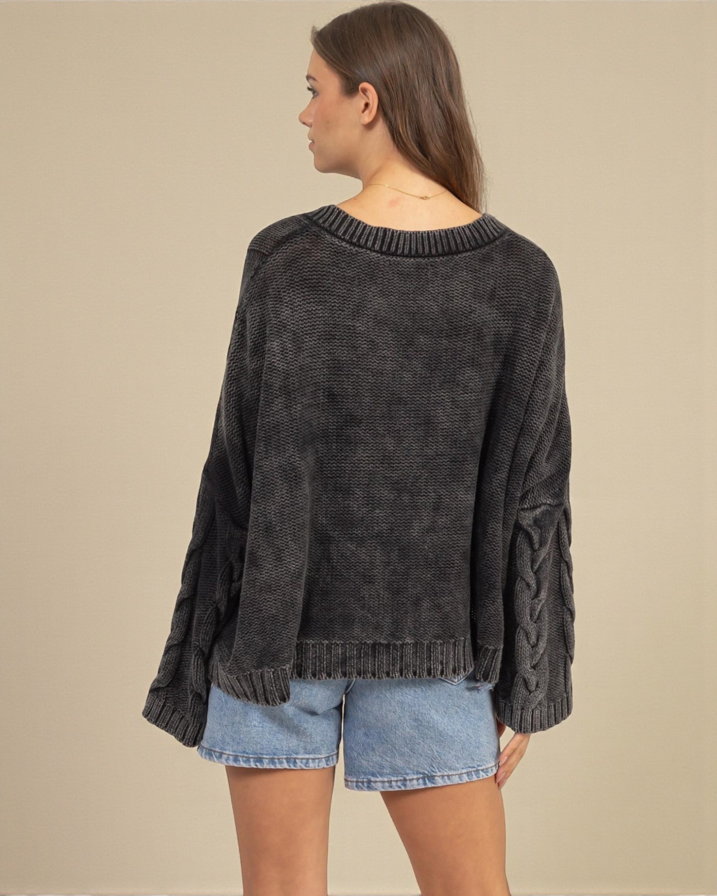 Woman wearing a dark gray sweater and denim shorts on a beige background