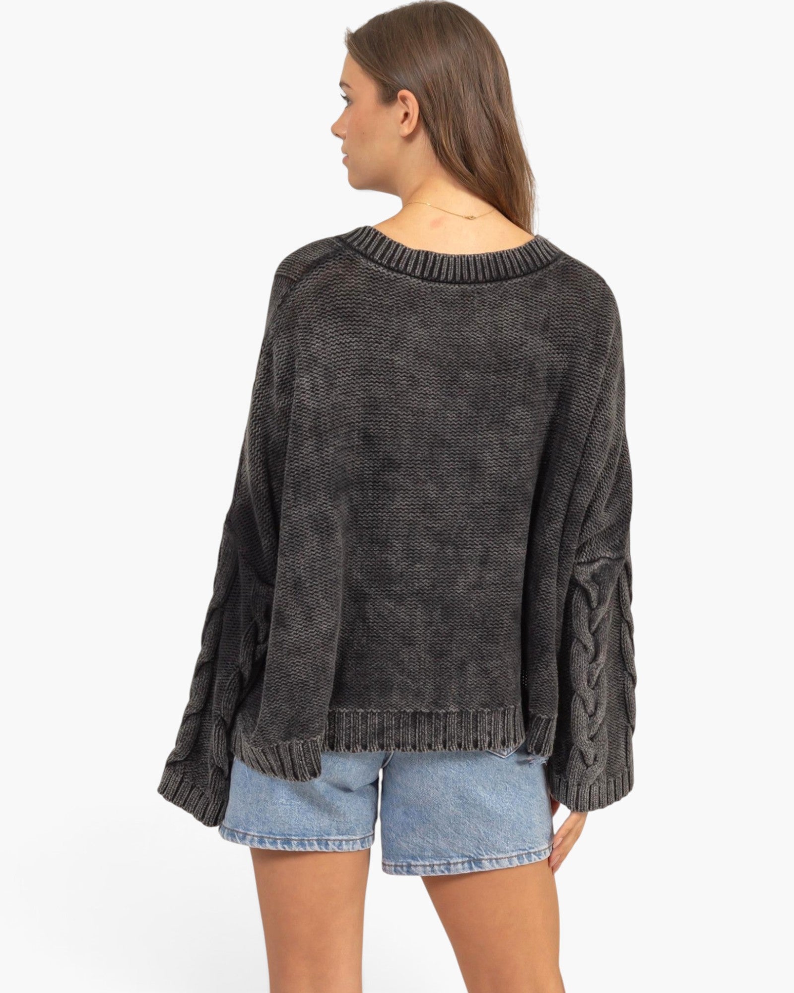 A woman shown from the back wearing a dark charcoal gray knit sweater with textured cable details on the sleeves, paired with light blue denim shorts, against a plain white background.
