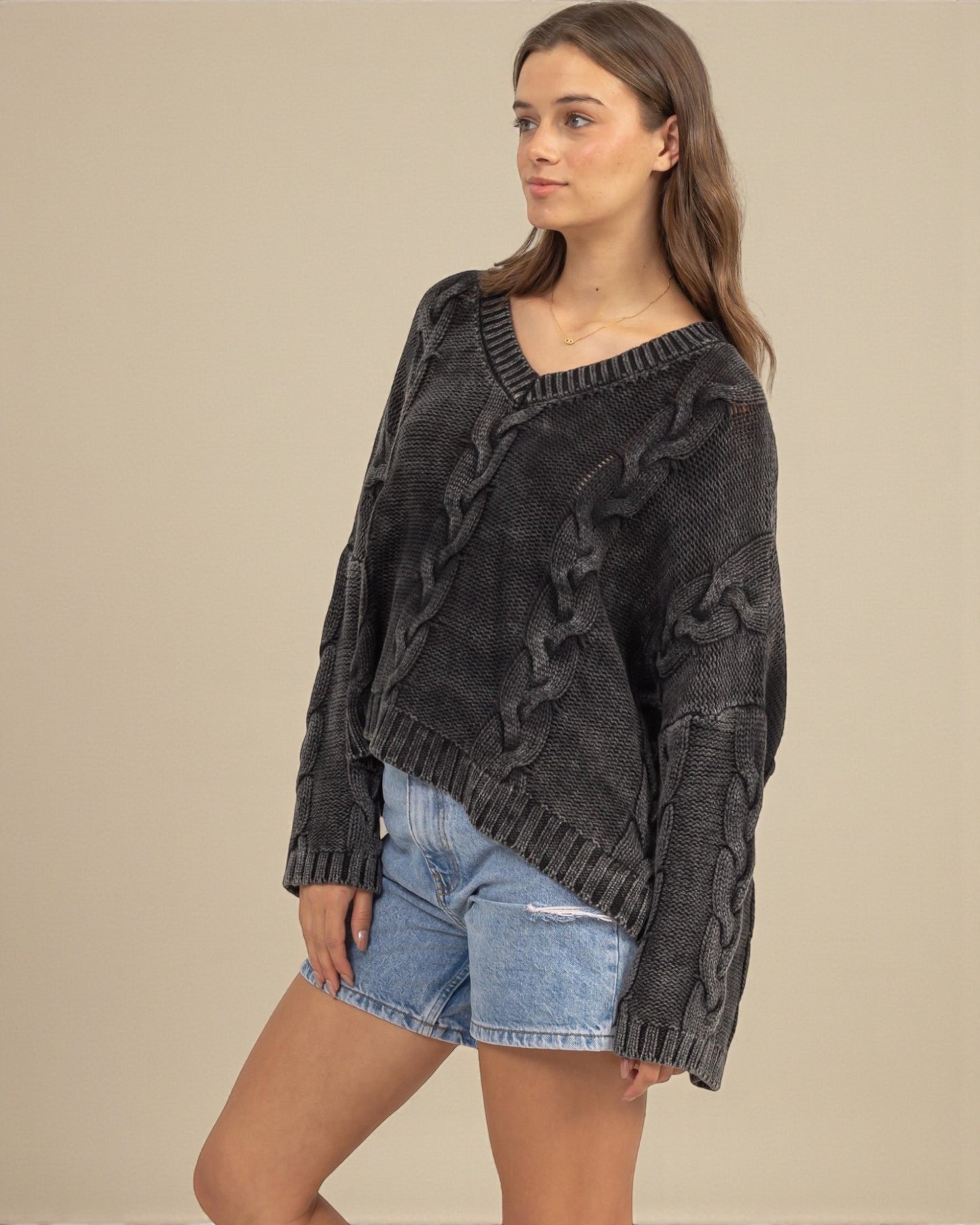 Woman wearing a dark gray cable knit sweater and denim shorts on a beige background