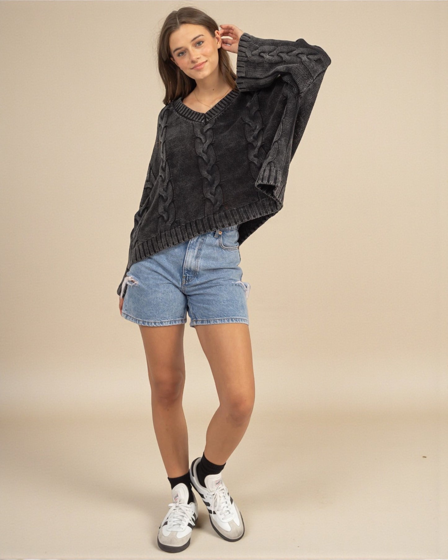 Woman wearing a dark gray cable knit sweater with denim shorts on a beige background