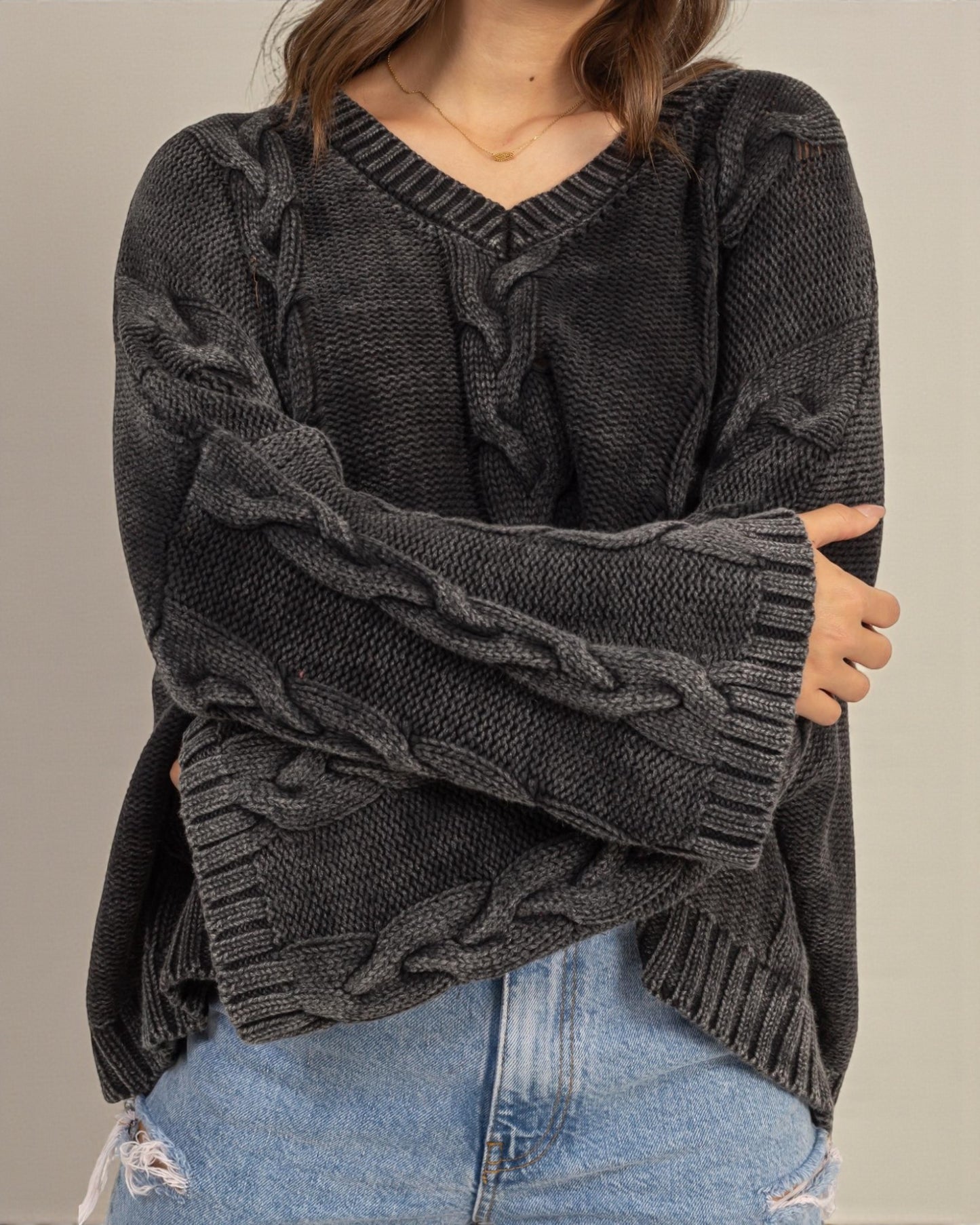 Person wearing a dark gray cable knit sweater with a plain background