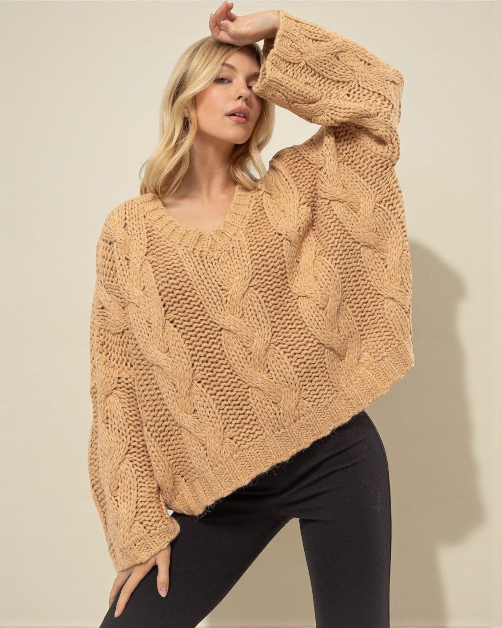 Woman wearing a beige cable knit sweater against a plain background