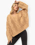 A woman wearing a chunky cable-knit cropped sweater in a warm camel tan color, paired with black pants, against a clean white background.