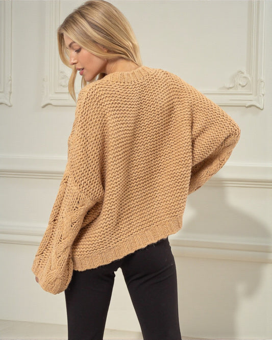Woman wearing a beige chunky knit sweater in a neutral setting