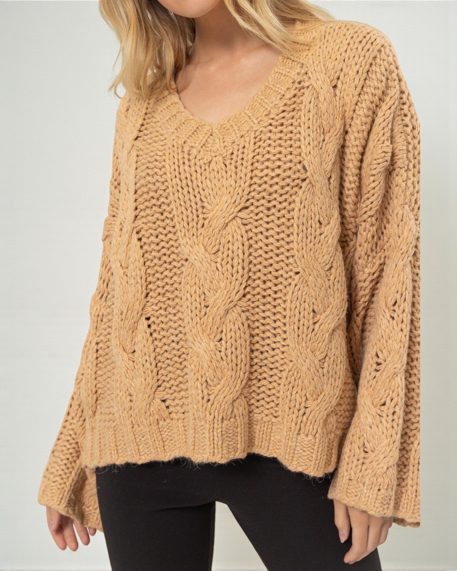 Beige knitted sweater worn by a person on a plain background