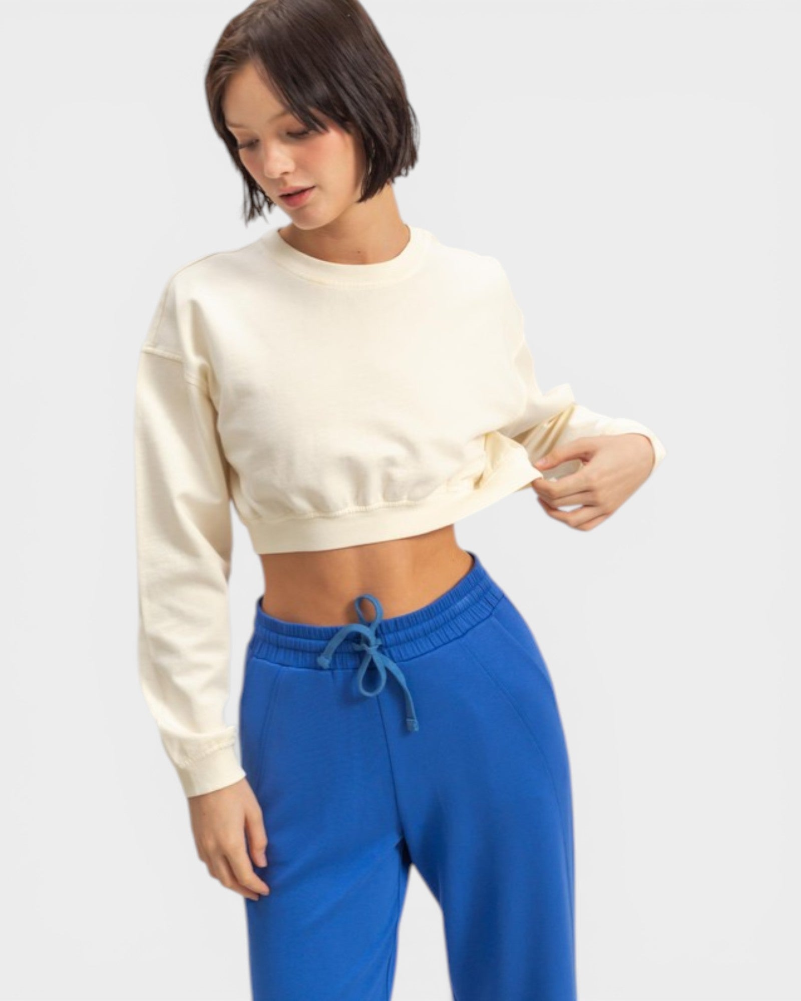 Woman wearing a beige cropped sweatshirt and blue pants on a light gray background