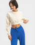 Woman wearing a beige cropped sweatshirt and blue pants on a light gray background