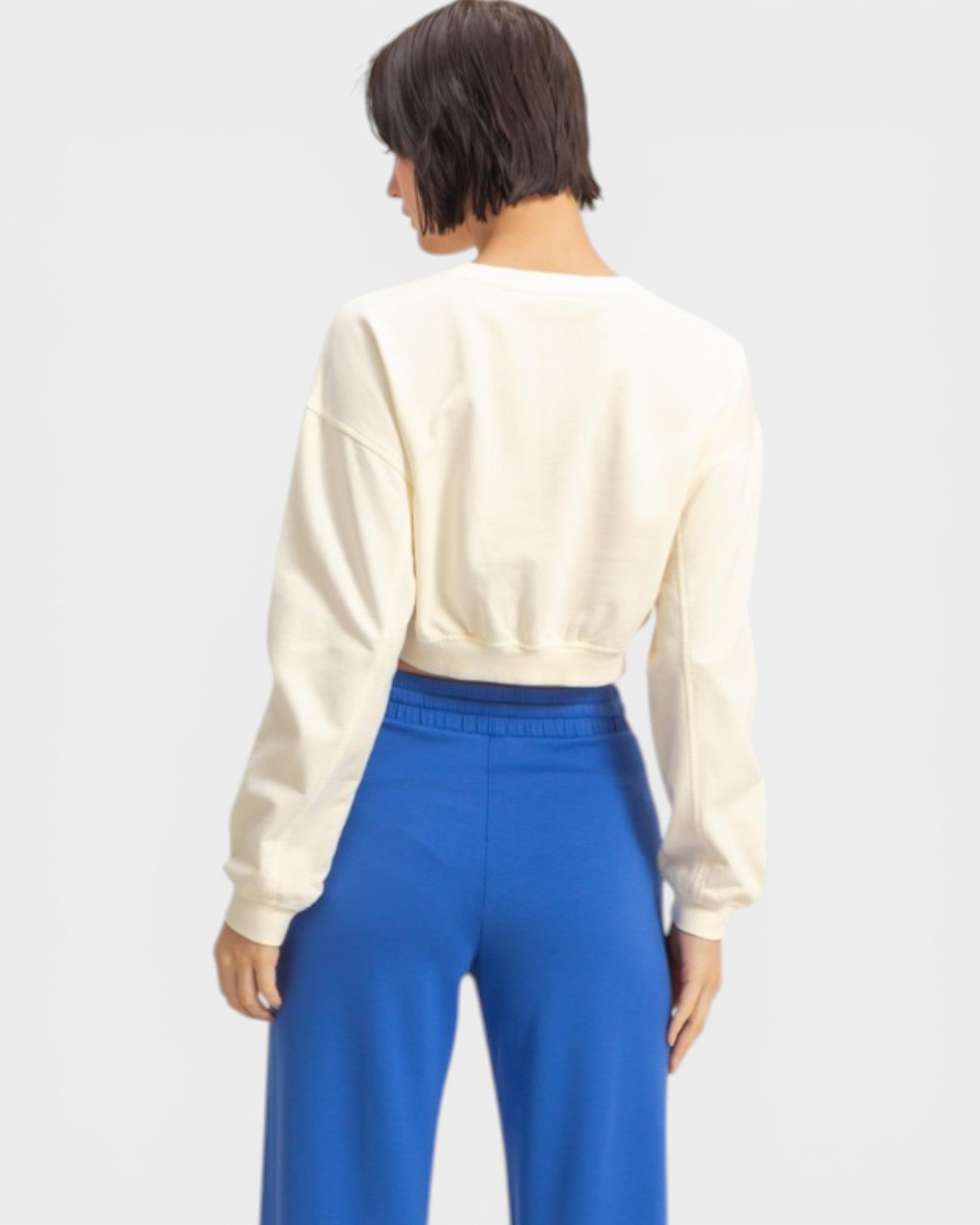 Person wearing a cream long-sleeve top and blue pants on a white background