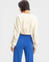 Person wearing a cream long-sleeve top and blue pants on a white background