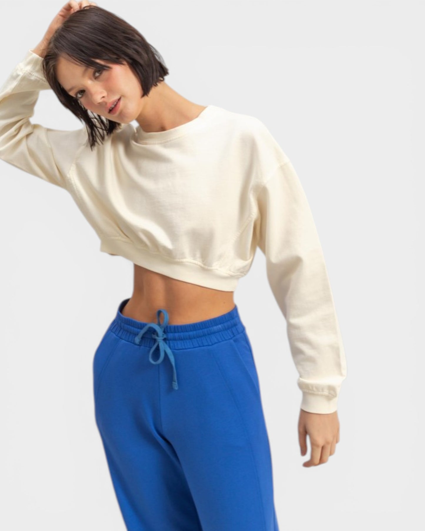 Woman wearing a cream sweatshirt and blue pants on a light gray background