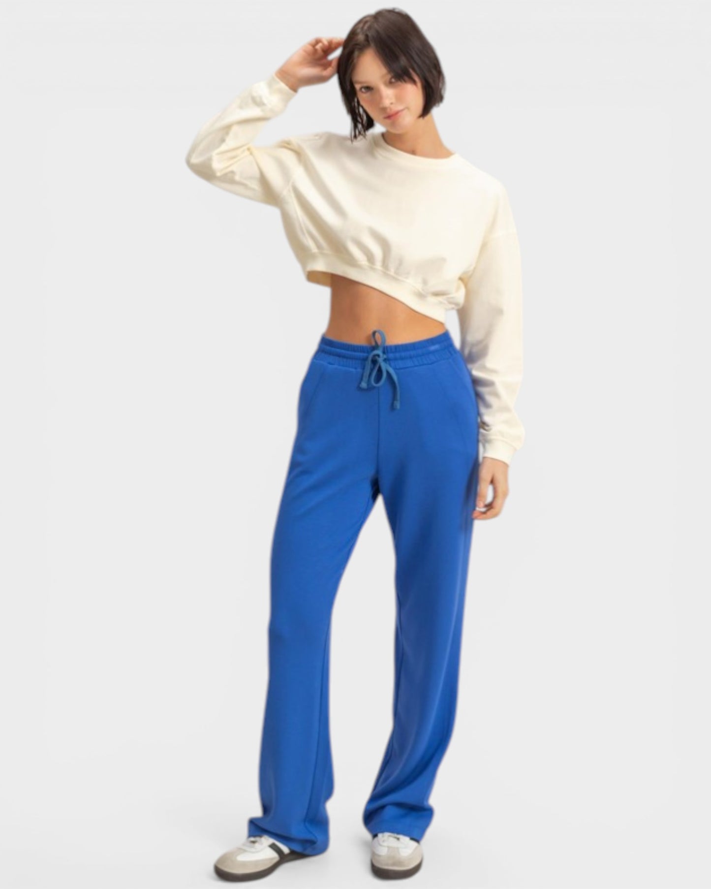 Person wearing a white cropped sweatshirt and blue pants on a white background