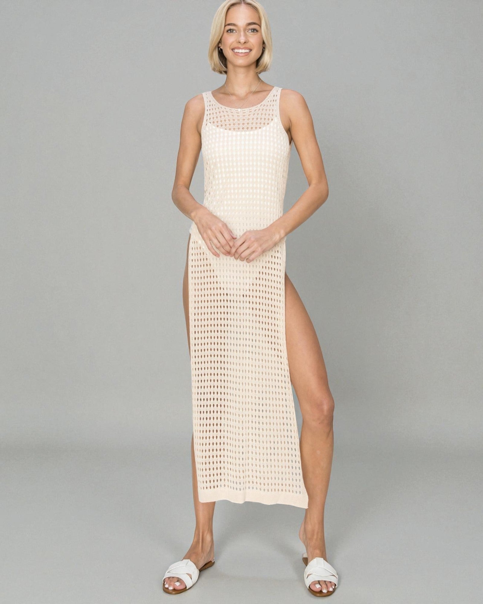 Woman wearing a beige crochet dress with a slit on a gray background