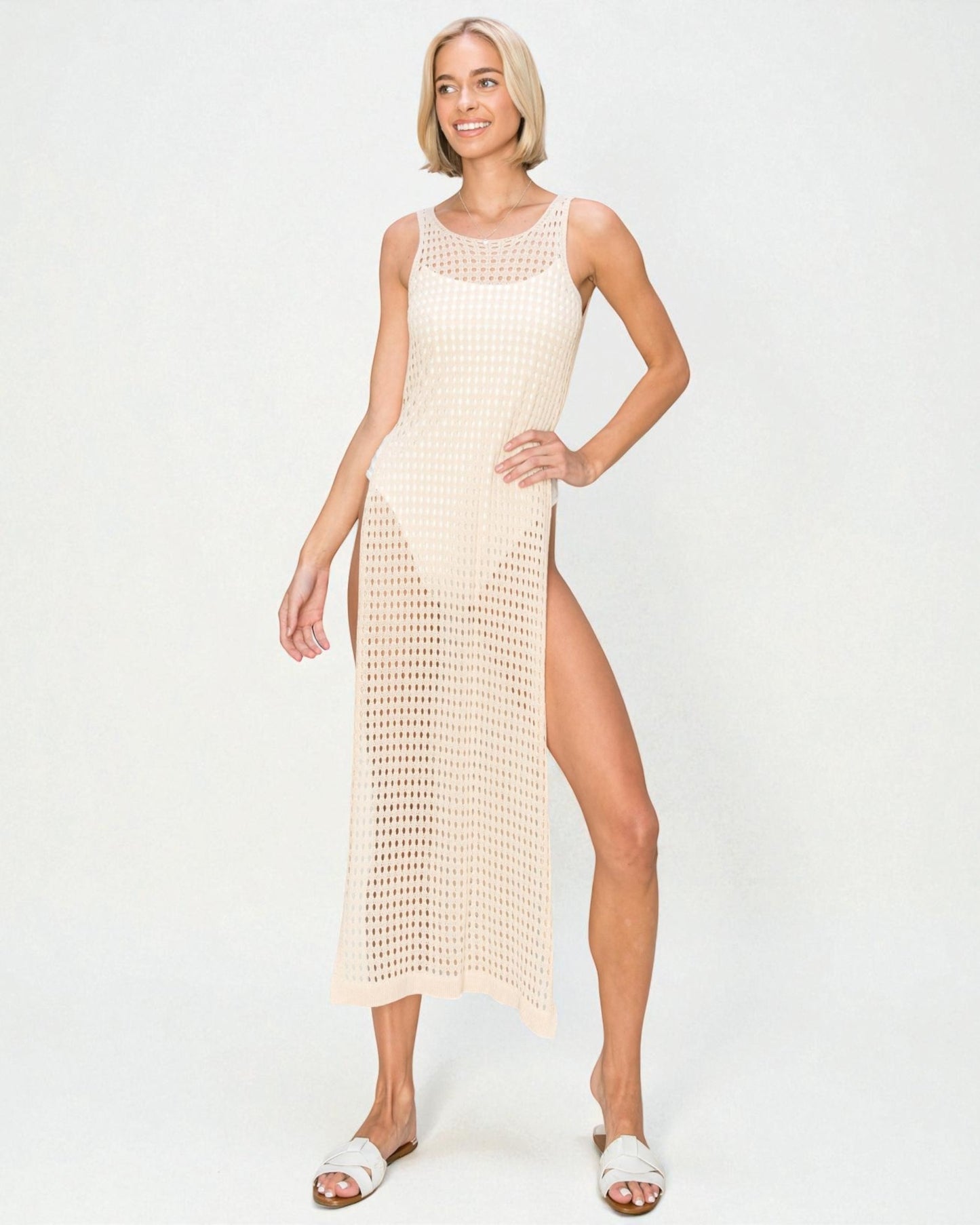 Woman wearing a beige crochet dress with a slit on a white background