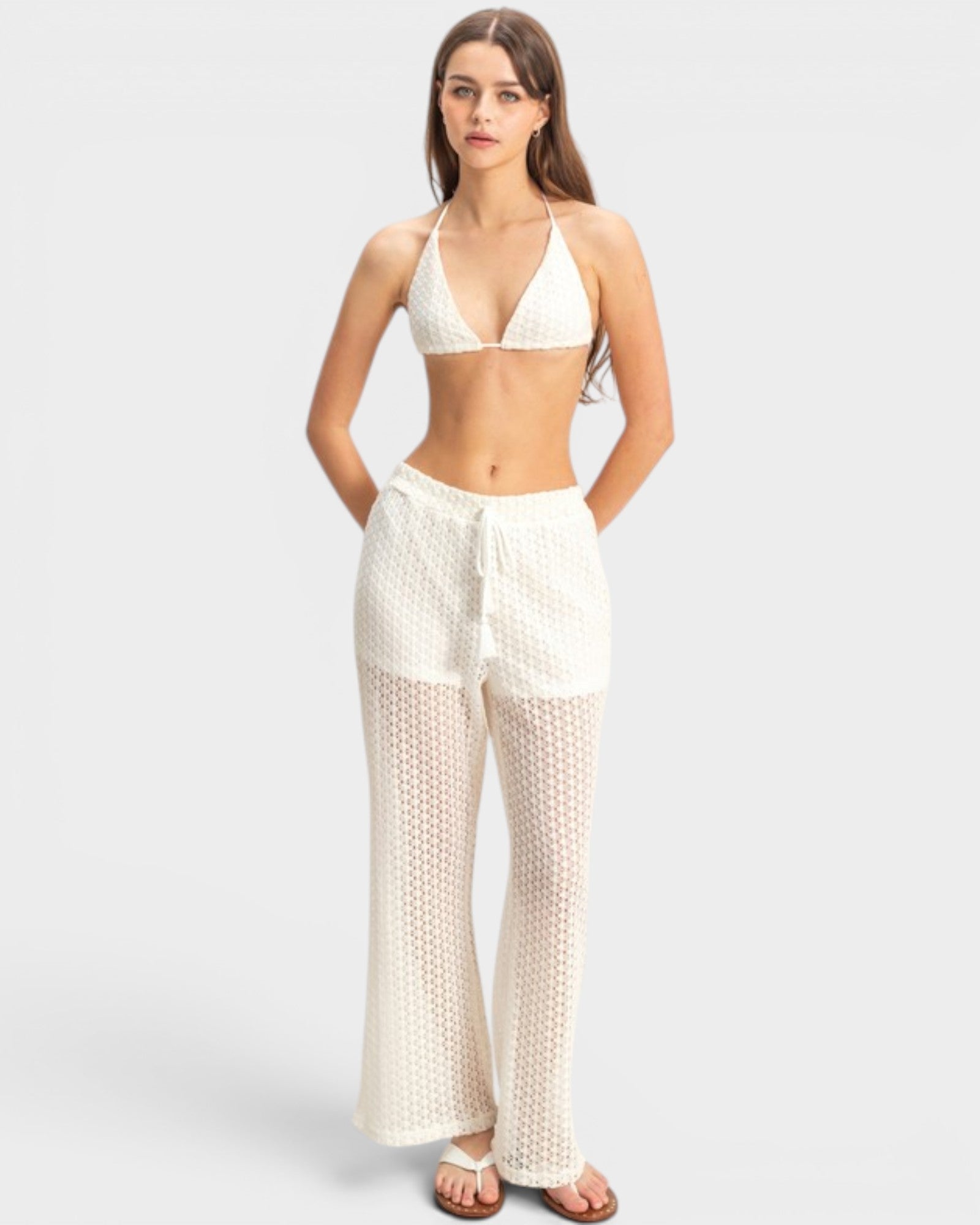 Woman wearing a white bikini and matching pants on a light gray background