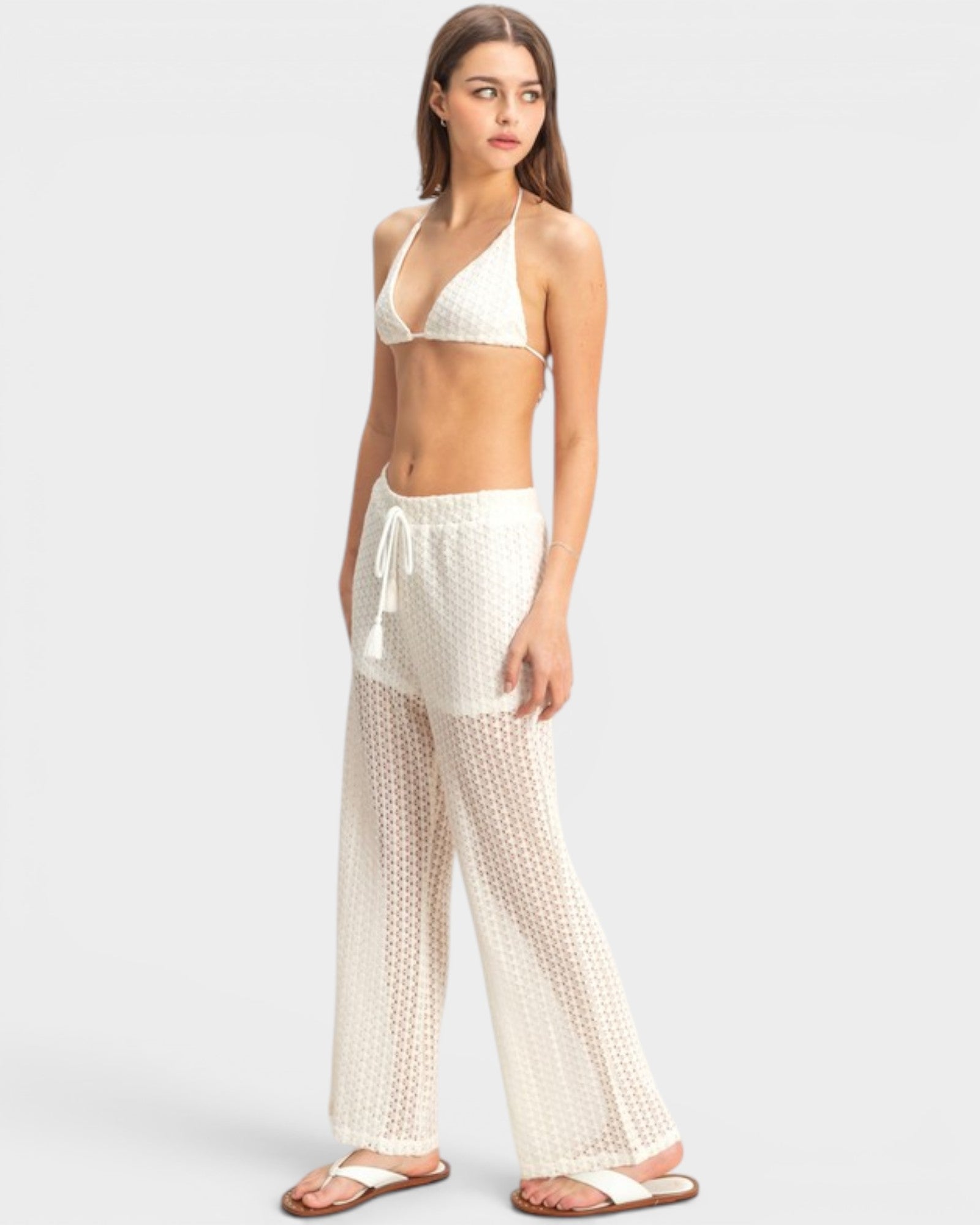 Woman wearing a white bikini set with matching pants on a light gray background