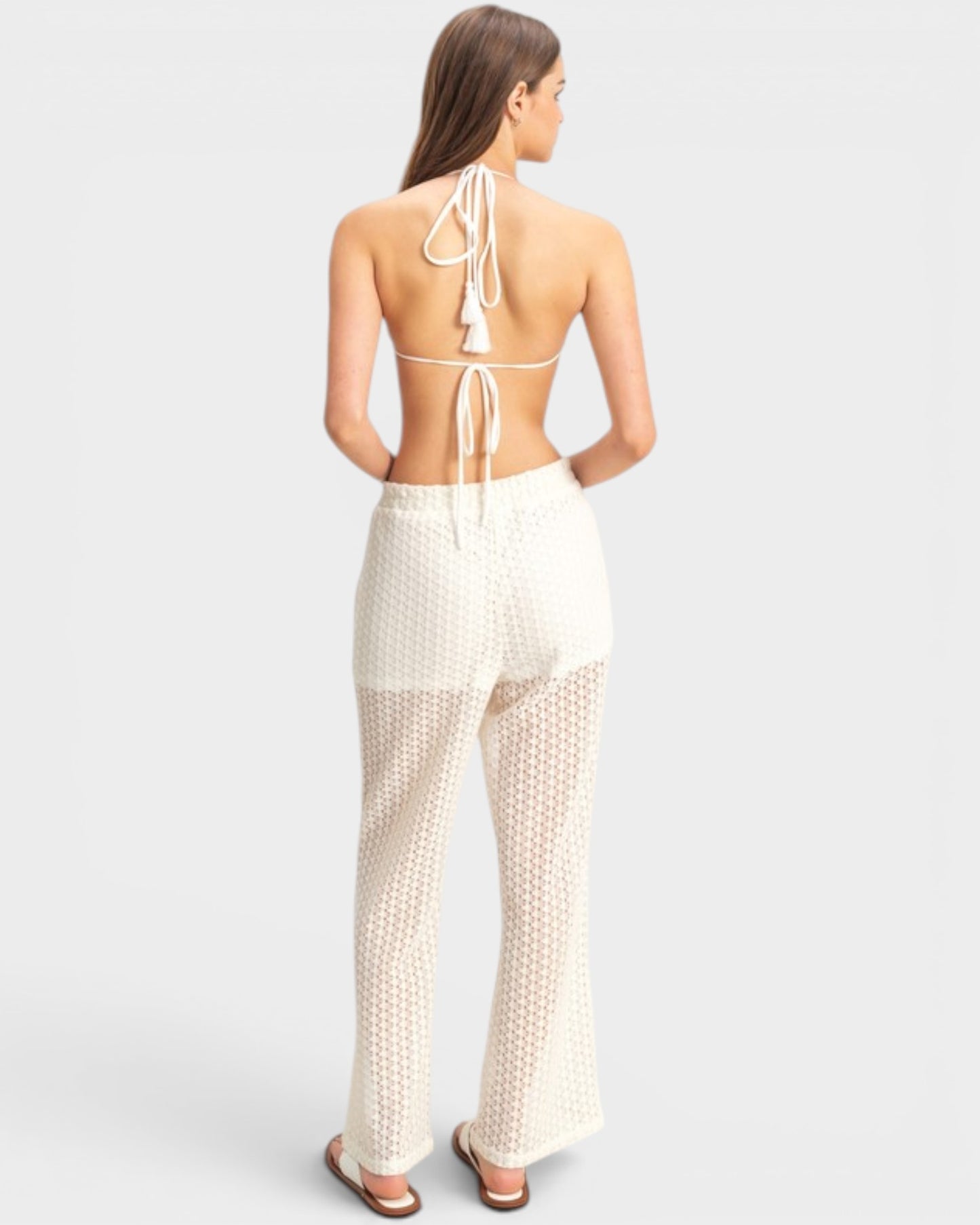 Woman wearing a white open-back top and matching pants on a light gray background