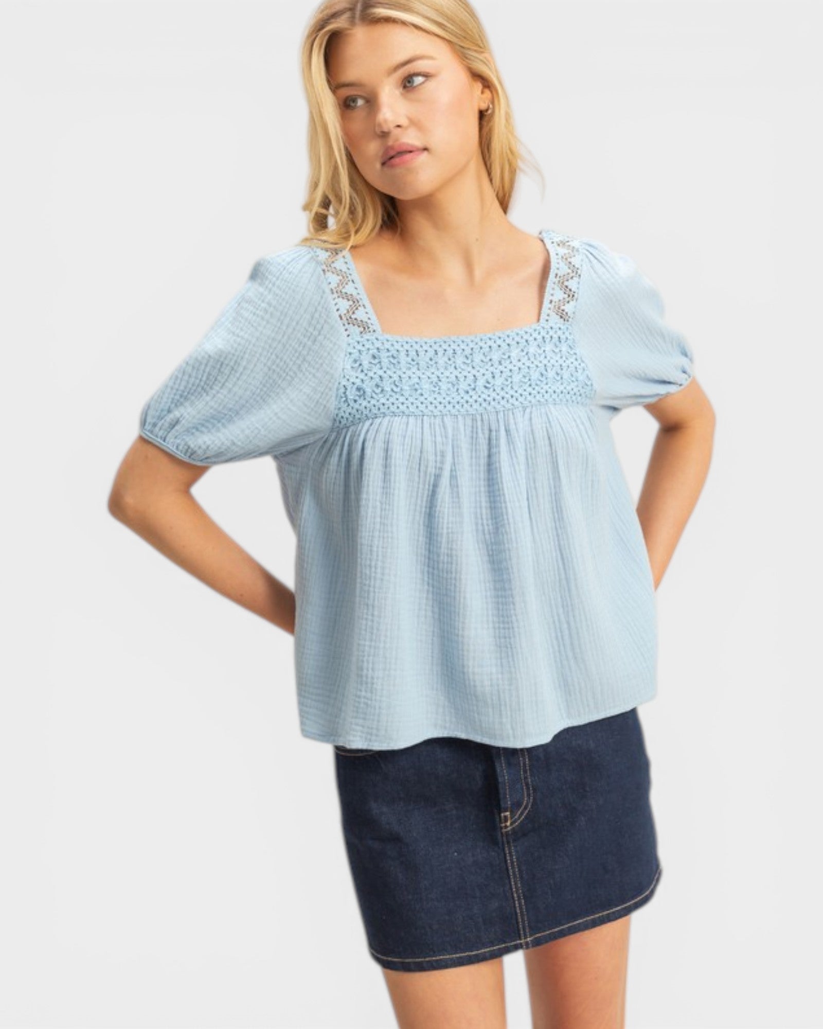 Woman wearing a light blue blouse with lace details and a denim skirt on a white background