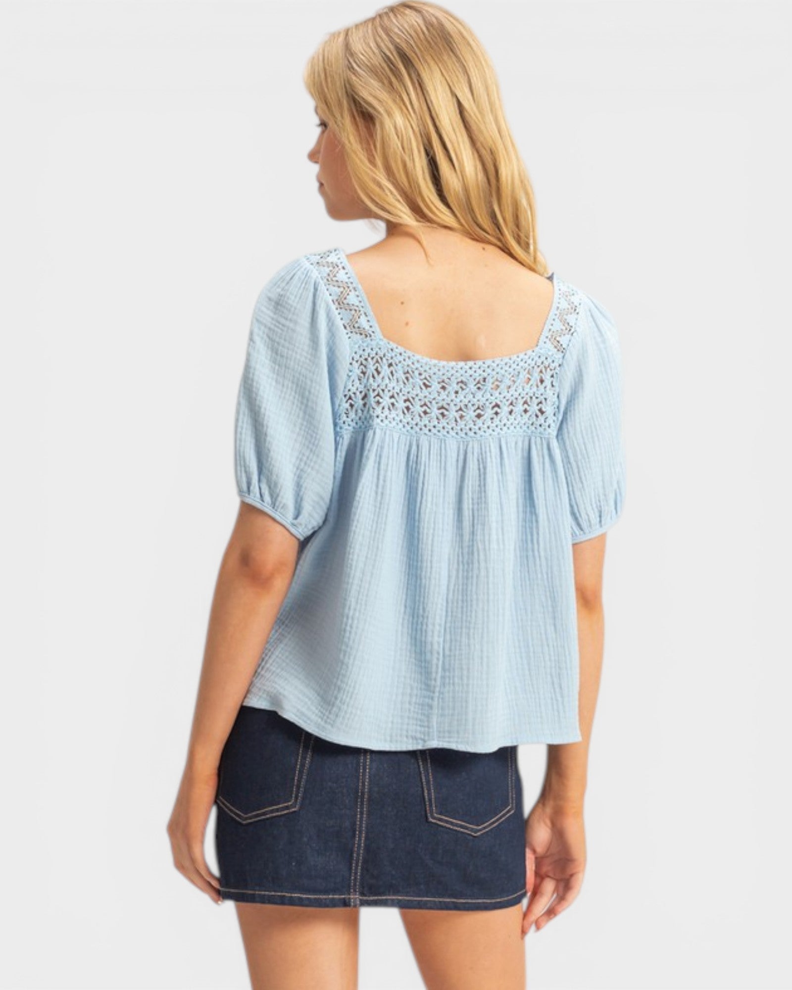 Woman wearing a light blue blouse with lace details and a denim skirt on a white background