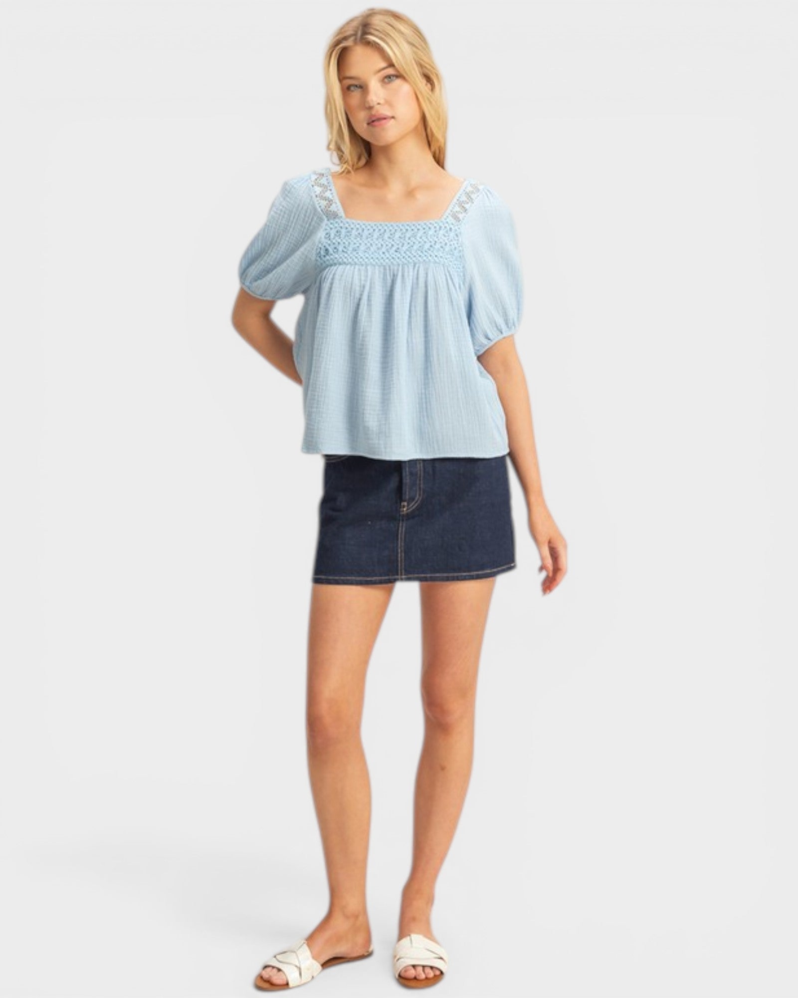 Woman wearing a light blue blouse and dark denim skirt on a white background