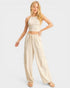 Woman wearing a beige halter top and wide-leg pants on a white background