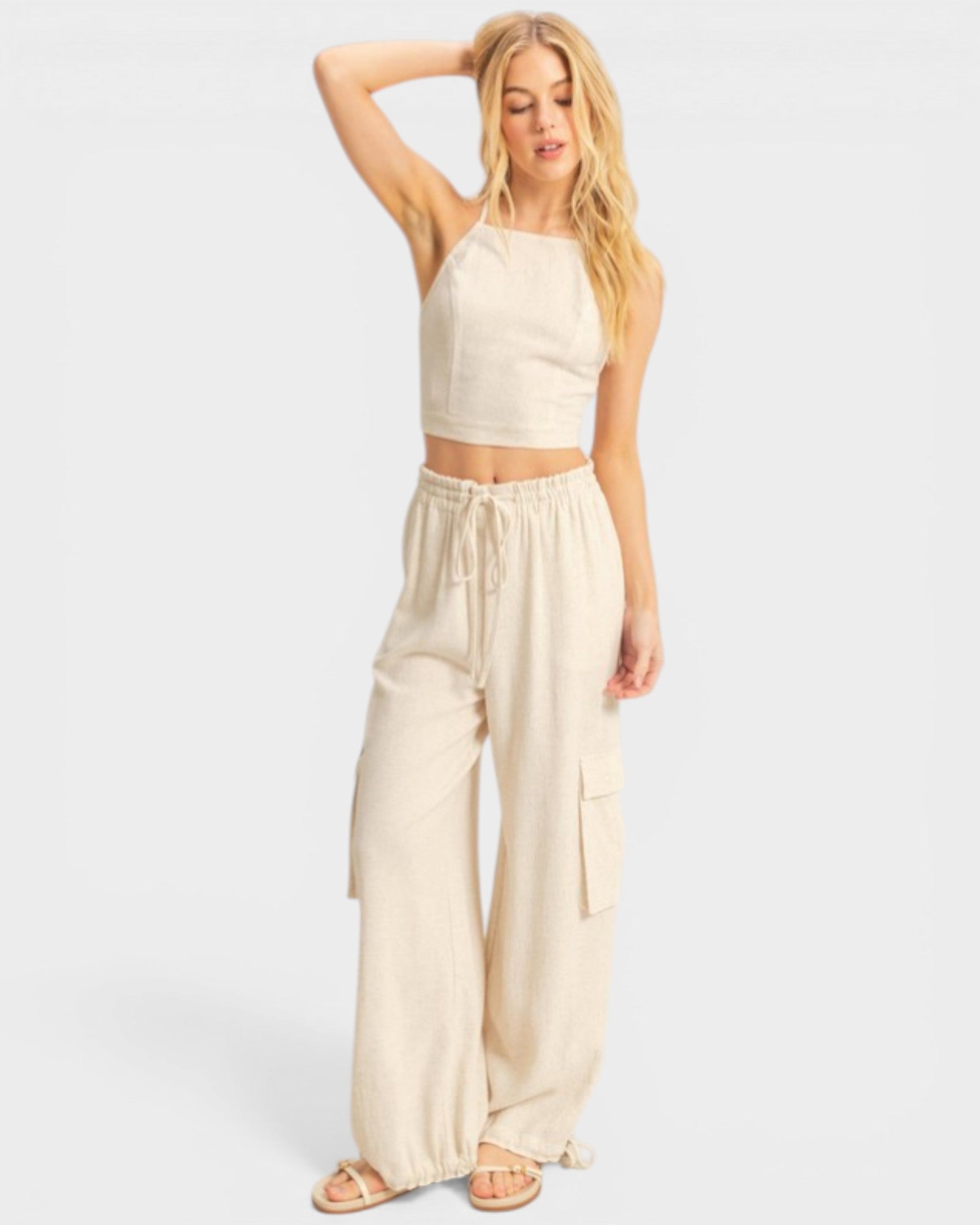 Woman wearing a beige sleeveless top and wide-leg pants on a white background