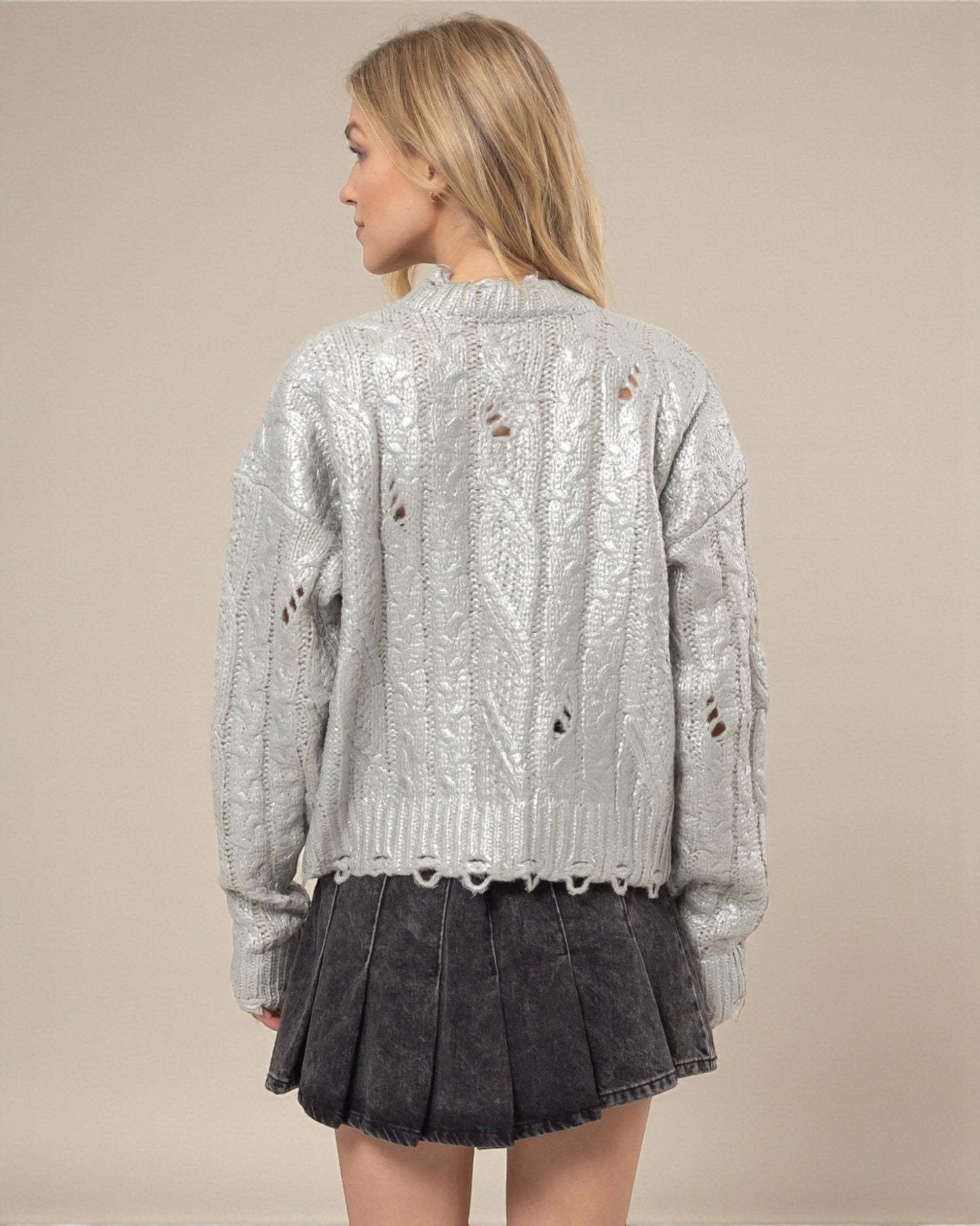 Woman wearing a silver sequin jacket and black pleated skirt on a beige background