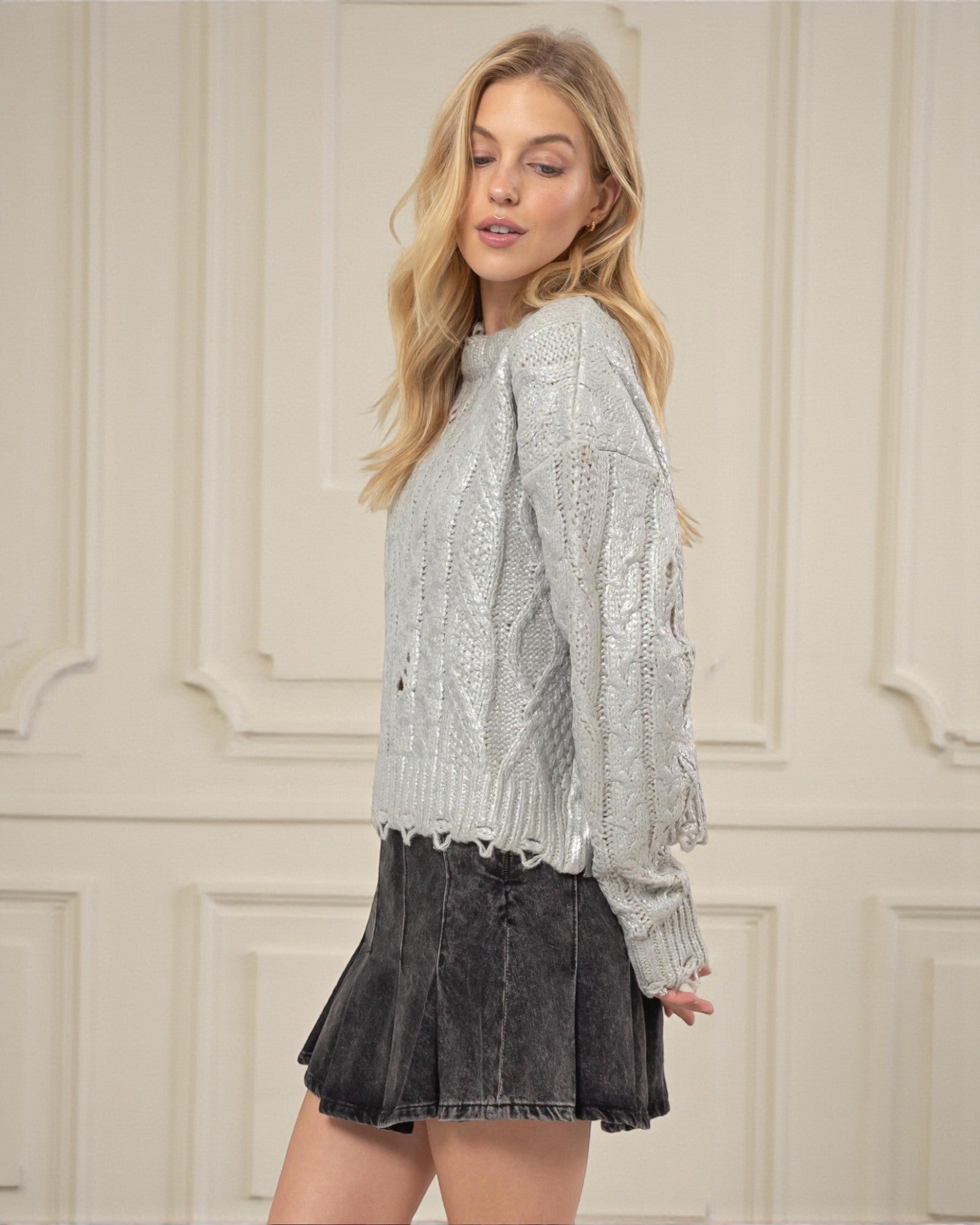 Woman wearing a silver sequin top and black skirt against a white paneled wall.