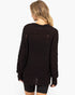 A woman viewed from the back wearing a dark brown chunky knit sweater with distressed details, paired with black shorts, against a plain white background.