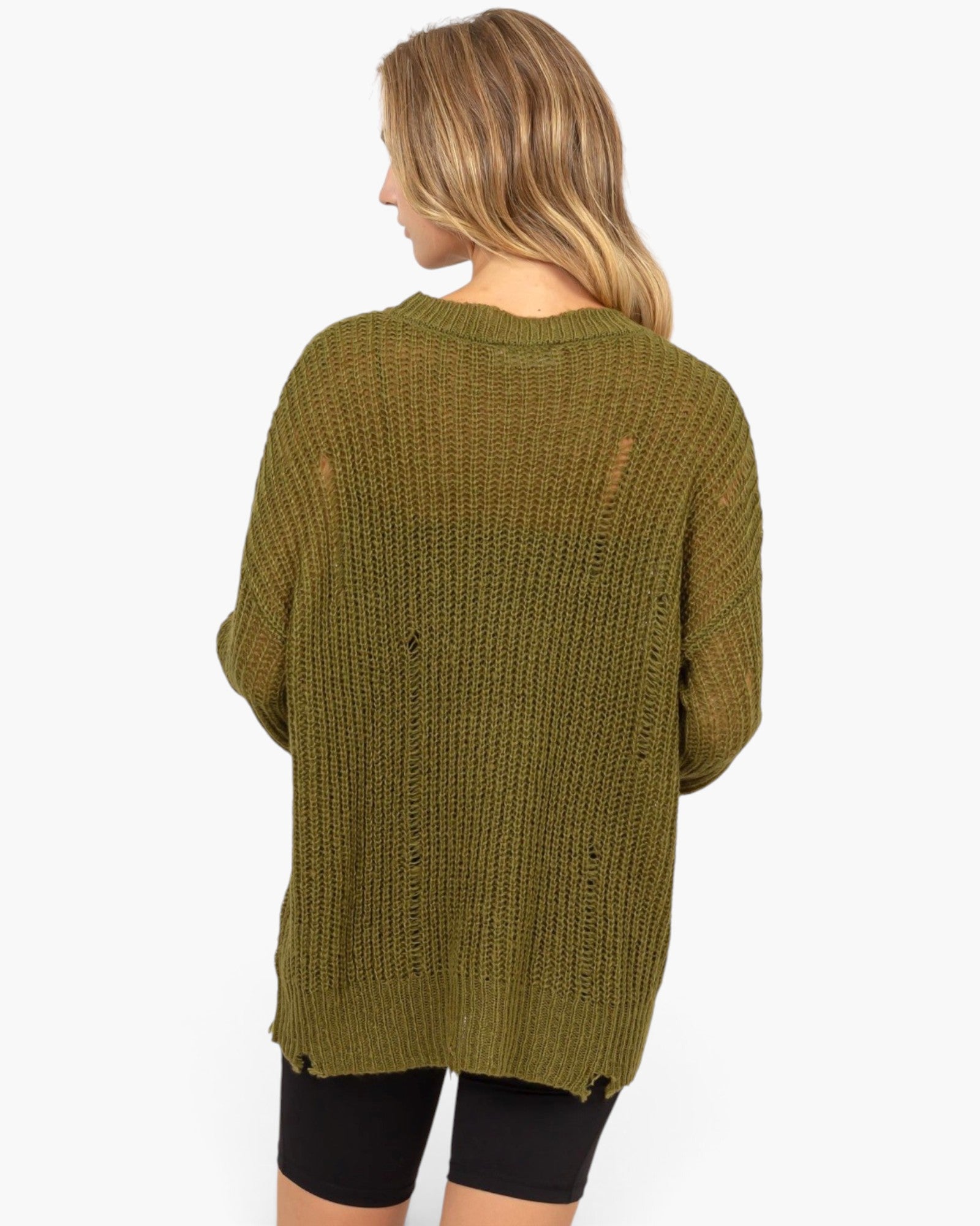 A woman shown from the back wearing an oversized olive green knit sweater with distressed details, paired with black shorts, against a plain white background.