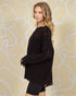 Woman wearing a black sweater and shorts against a beige wall with white abstract patterns