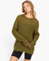 A woman wearing an oversized olive green chunky knit sweater with black bike shorts, photographed against a clean white studio background.