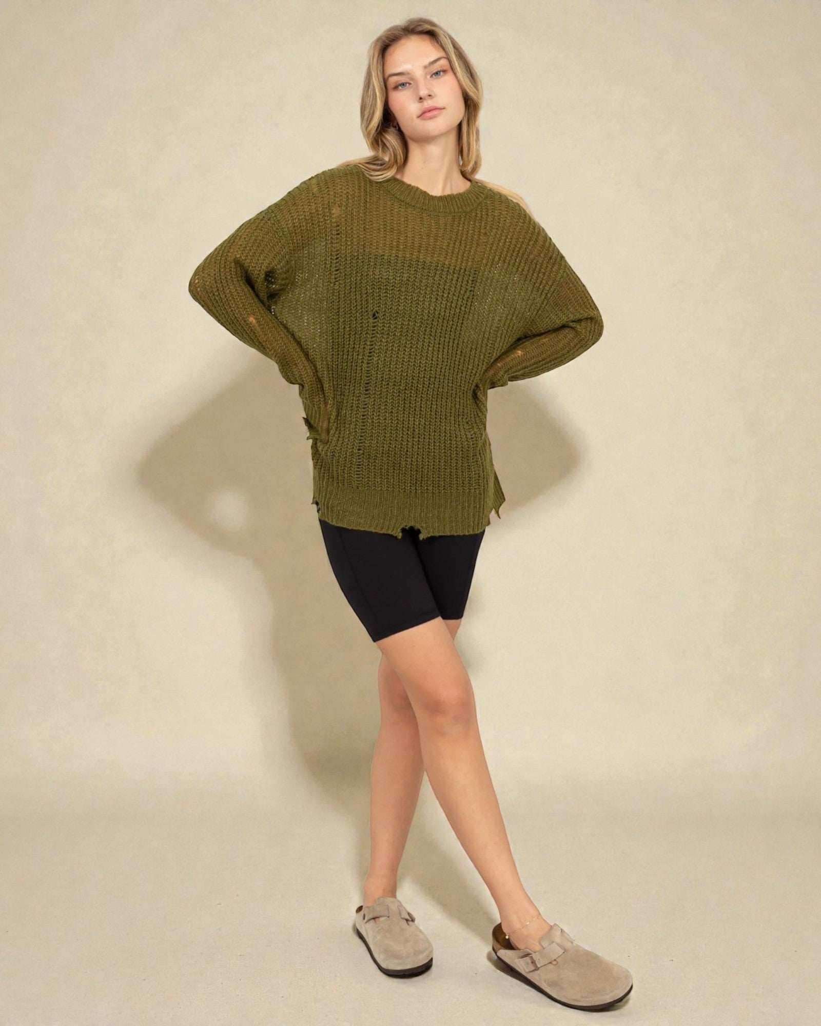 Woman wearing a green oversized sweater and black shorts on a beige background