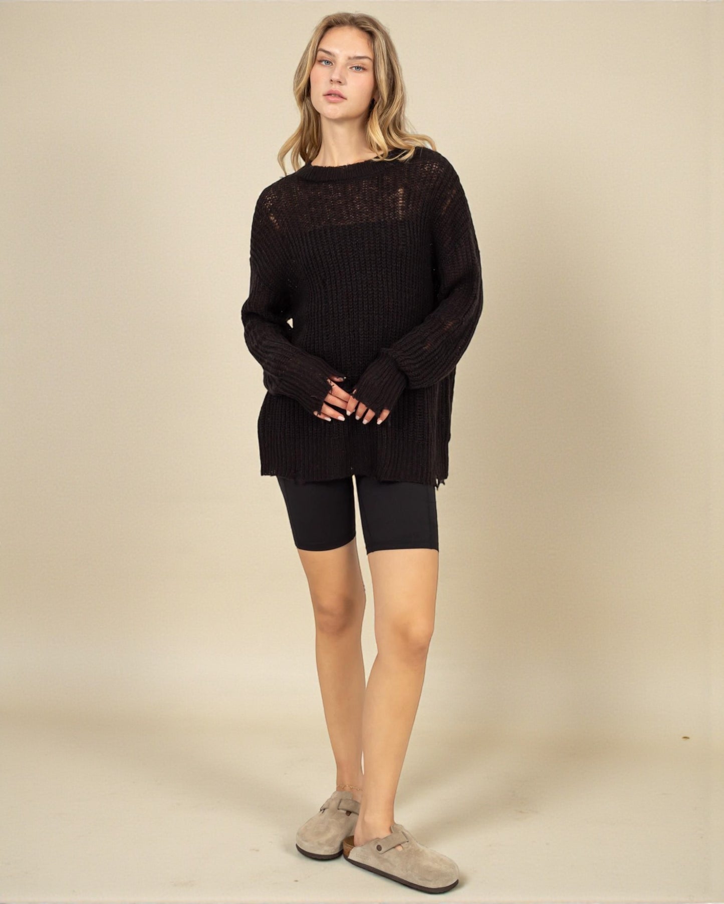 Woman wearing a black sweater and black shorts on a beige background