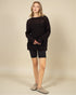 Woman wearing a black sweater and black shorts on a beige background