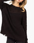 A close-up of a woman wearing a dark brown open-knit crewneck sweater, showing the textured knit pattern and frayed hem against a plain white background.