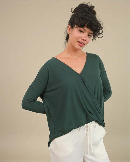 Woman wearing a green long-sleeve top with a V-neckline against a beige background