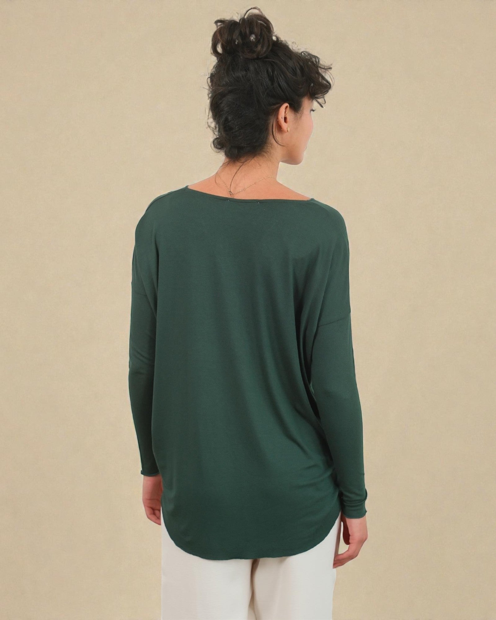 Woman wearing a green long-sleeve top against a beige background