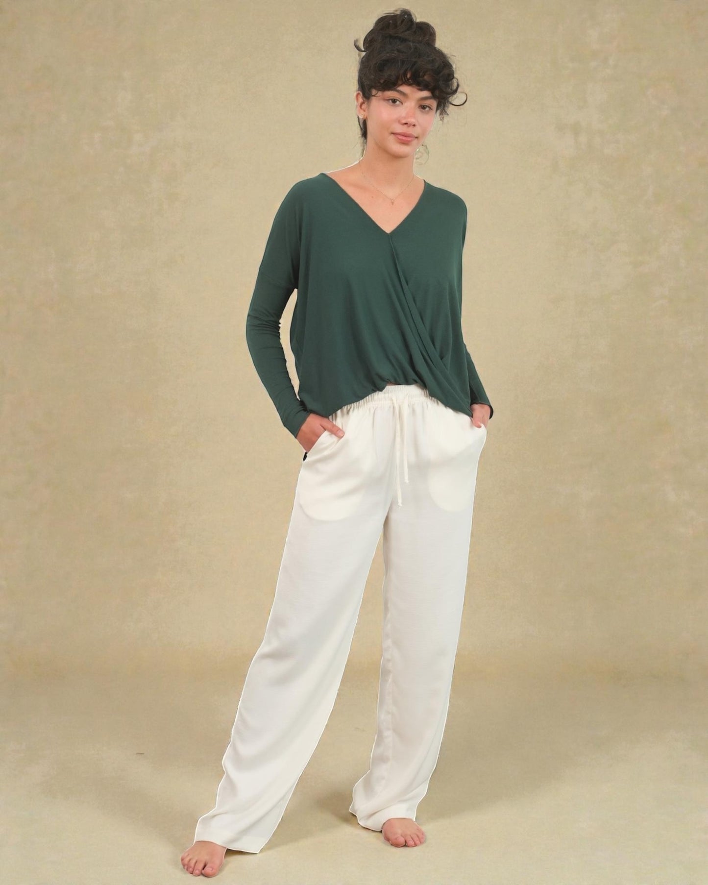 Person wearing a green top and white pants against a beige background