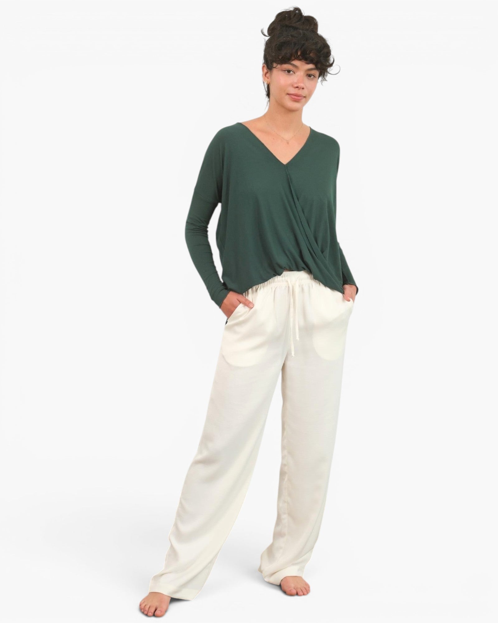 A woman modeling a dark green long-sleeve V-neck top paired with cream-colored wide-leg pants, standing against a plain white studio background.